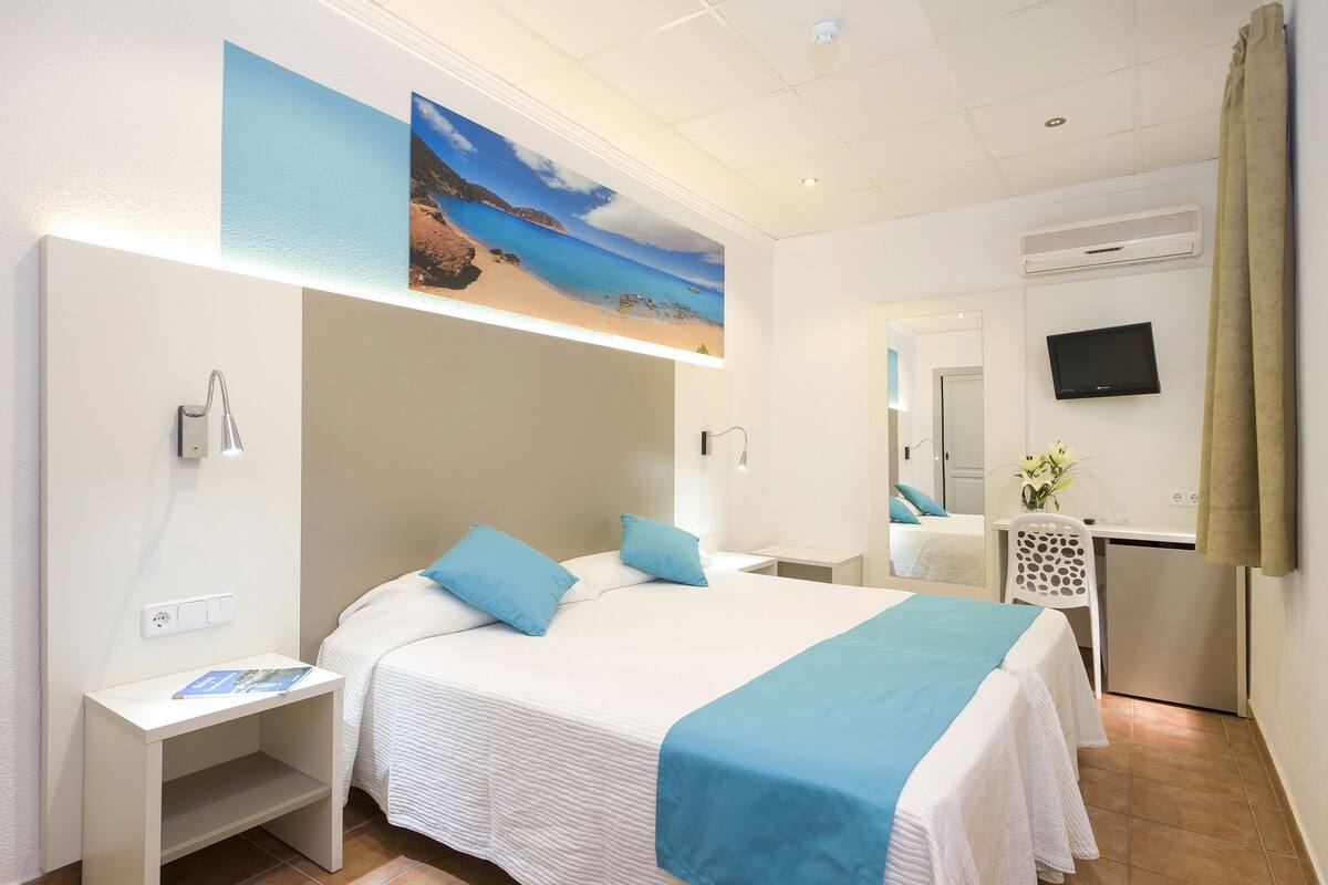 Ein Hotelzimmer mit einem Bett, einem Schreibtisch, einem Stuhl, einem Fernseher und einem Bild von einer Strandlandschaft.