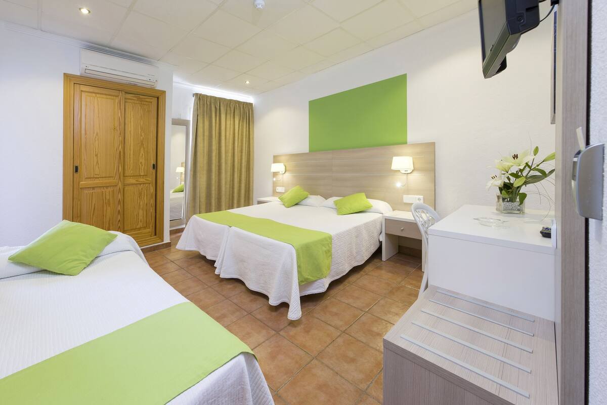 Ein Hotelzimmer mit zwei Betten, einem Schreibtisch, einem Stuhl, einem Fernseher und einem durch eine Tür einsehbaren Badezimmer.