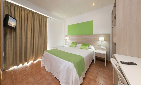 A hotel room with a bed, bedside tables, a TV, and a green accent wall.