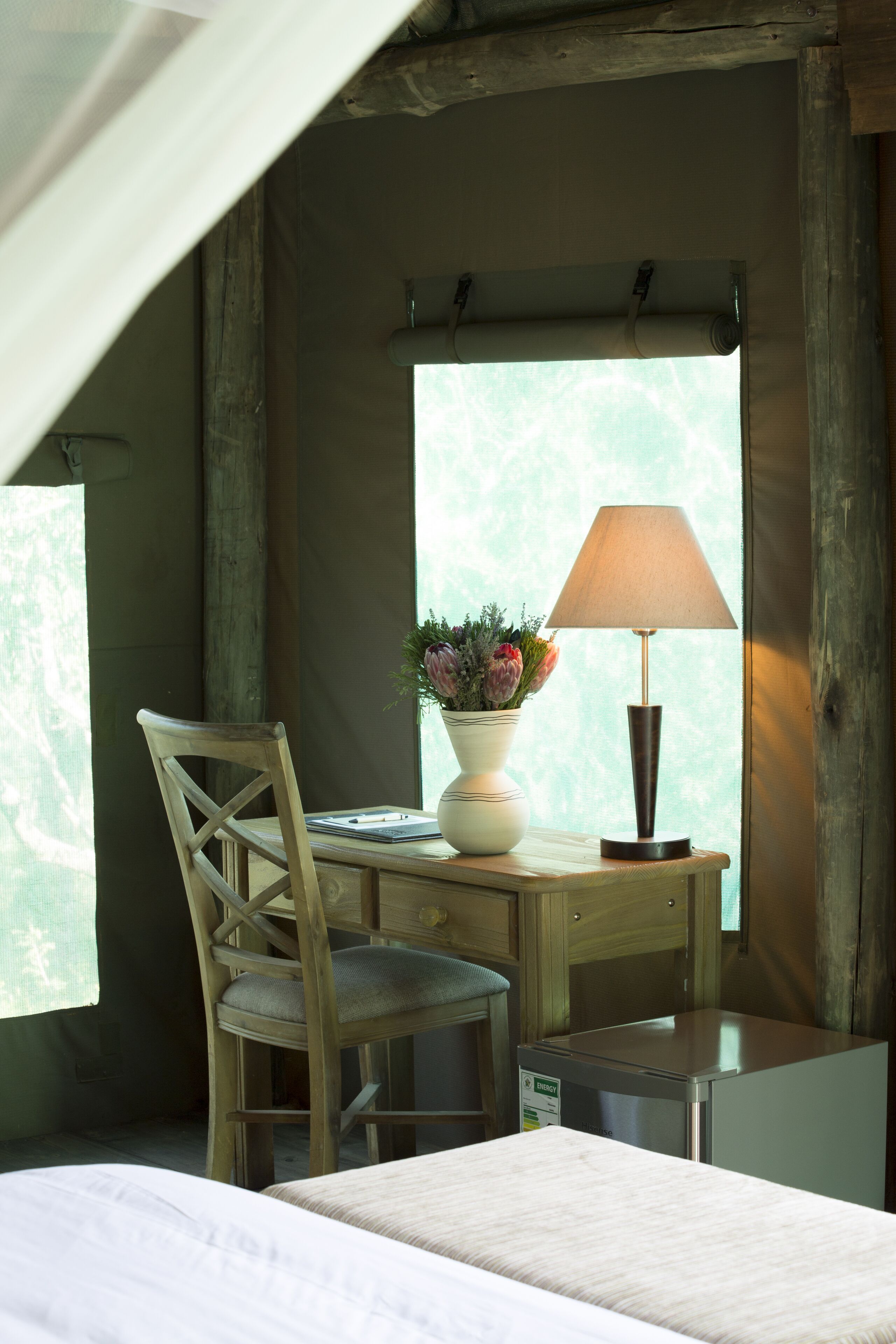 Ett skrivbord i trä med en lampa, en stol och en vas med blommor.