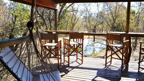 A wooden deck with a hammock, wooden chairs, and tables overlooking a natural landscape. - Honeyguide Ranger Camp (Mookgopong)