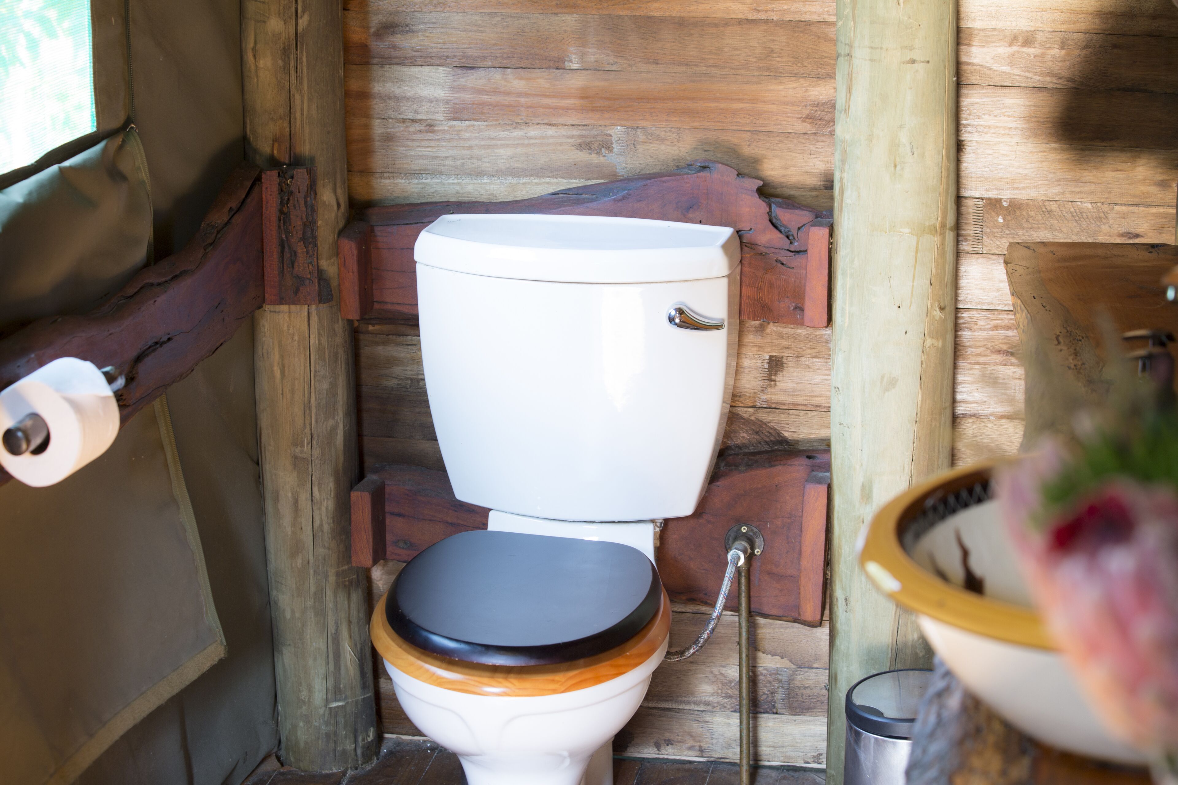 A rustic wooden bathroom with a white toilet, wooden seat, and a metal bidet.
