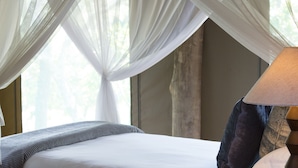 A bed with a white bedspread, a wooden headboard, and a bedside table with a lamp. - Honeyguide Ranger Camp (Mookgopong)