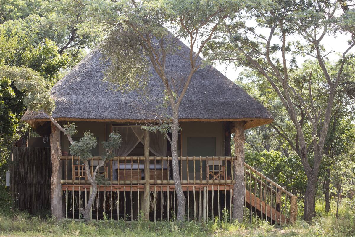 A thatched-roof structure with a wooden deck and a staircase leading to a balcony.