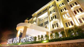 Un hotel con un cartel llamativo que dice "SYLVIA HOTEL" y una fachada bien iluminada con varias ventanas.