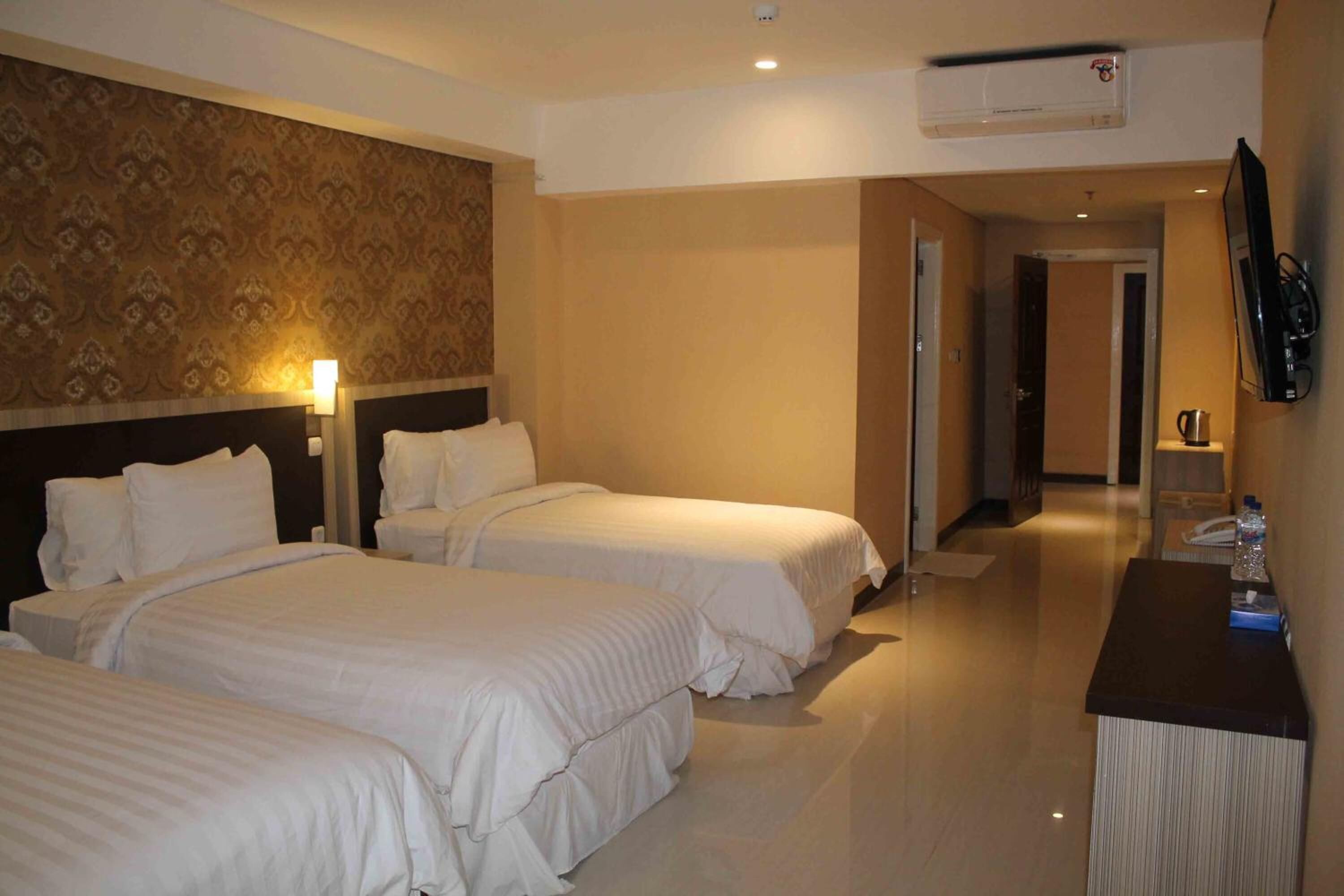 A hotel room with two beds, a desk with a chair, a mirror, and a wall-mounted TV.