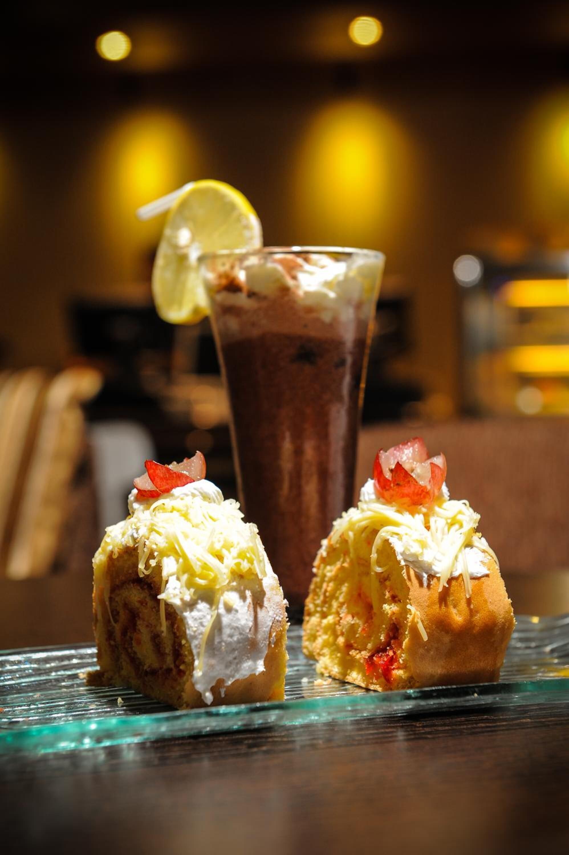 Deux desserts présentés sur une assiette en verre, avec une boisson au chocolat en arrière-plan.