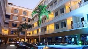 Un hôtel à plusieurs étages doté de balcons, d’un espace piscine et de palmiers.