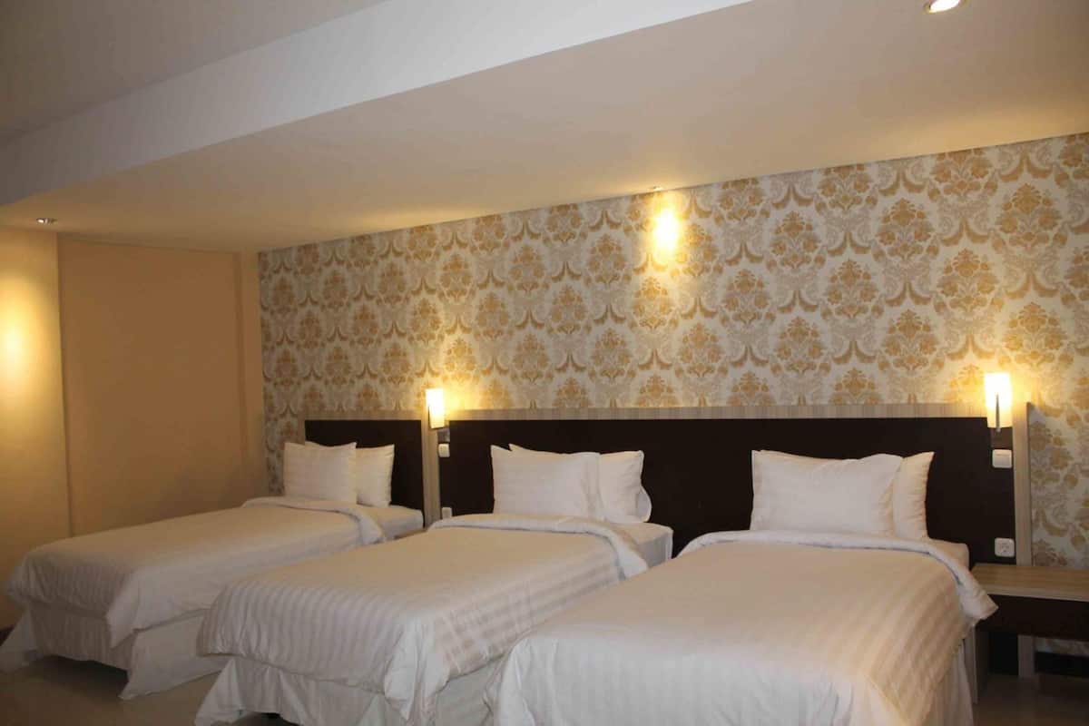 Een hotelkamer met drie enkele bedden, een donker hoofdbord en behang met een patroon.