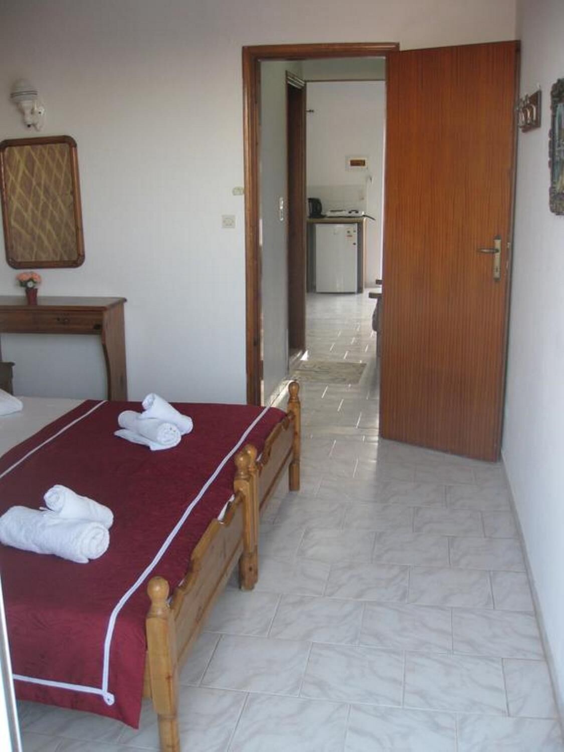 A hotel room with a wooden bed, a red bedspread, and a tiled floor.