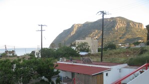 Edifici costaner amb teulada vermella, envoltat de vegetació i un paisatge de muntanyes al fons.
