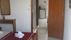 Habitació d'hotel amb un llit, una petita taula de nit de fusta, una taula petita amb un ram de flors i una porta que dona a una zona de cuina.