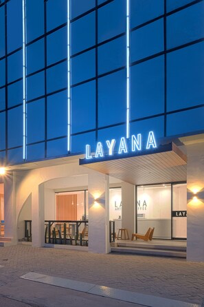 A modern building with a 'LAYANA' sign, featuring a glass facade and a welcoming entrance with steps and seating.