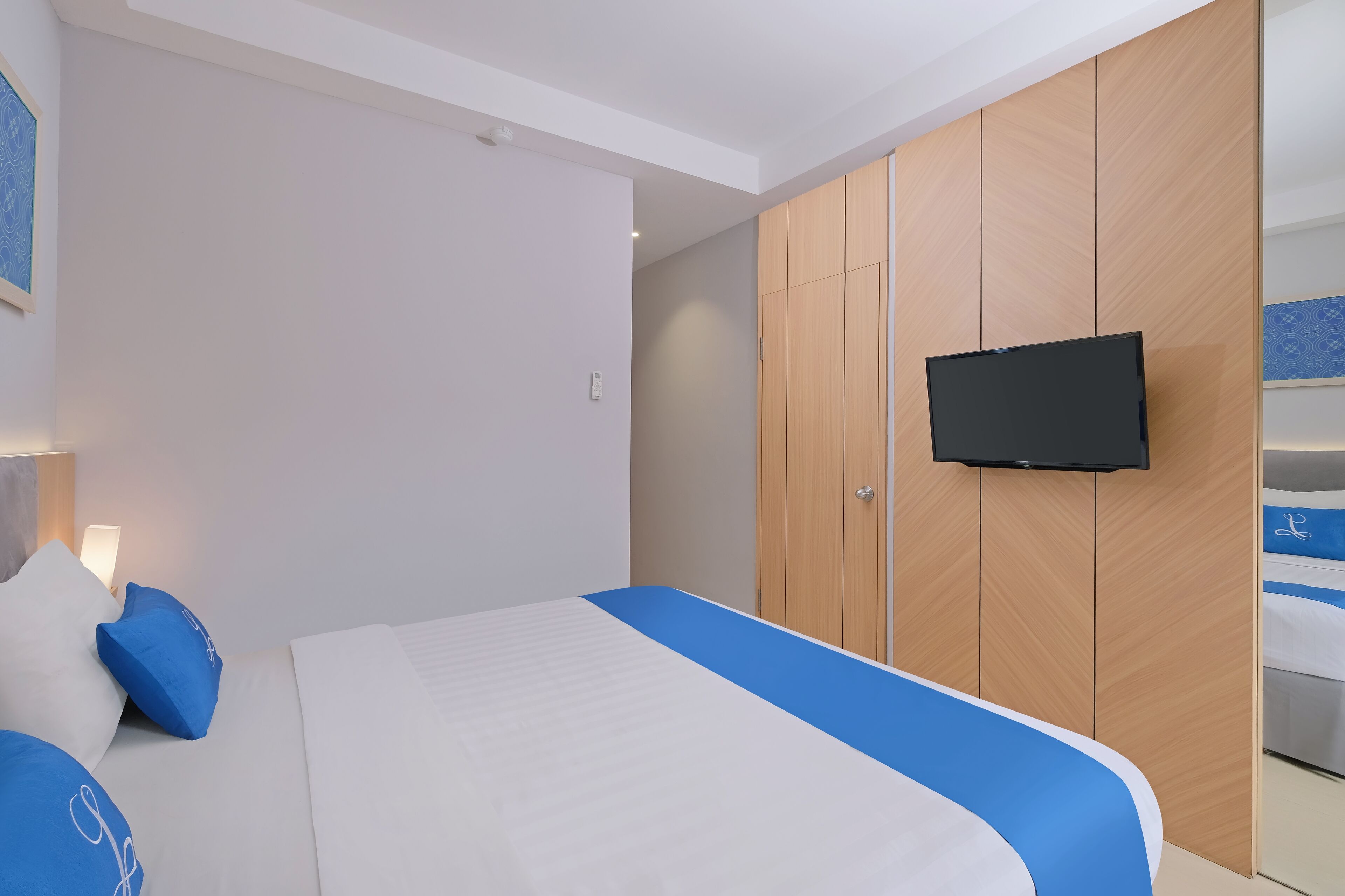 Ein Hotelzimmer mit einem Bett, einem an einer Holzkommode befestigten Fernseher und einem Nachttisch mit einer Lampe.