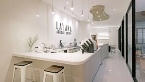L’intérieur d’un café moderne présente un comptoir central, deux tabourets et un panneau affichant le menu.