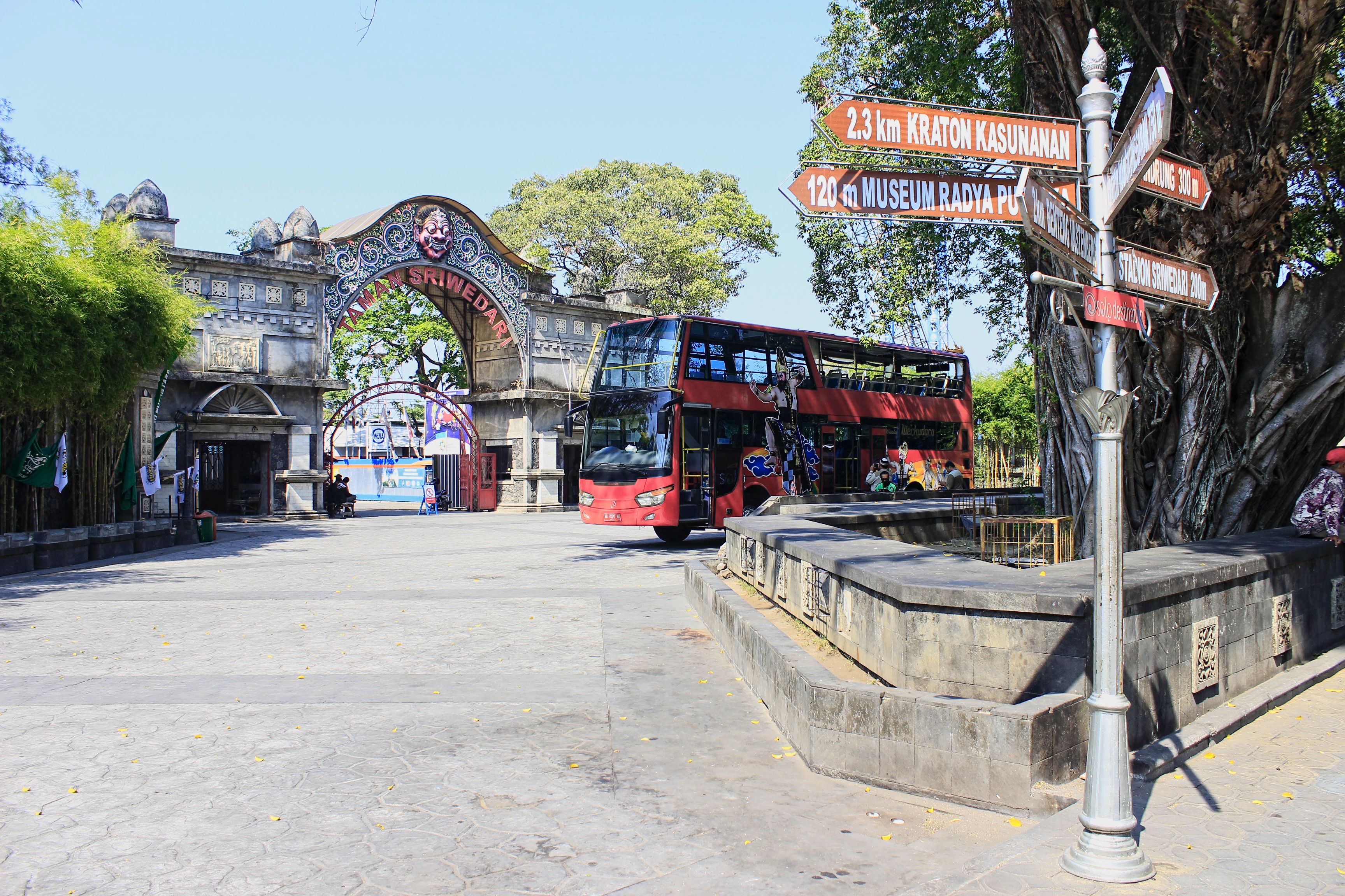 A red double-decker bus at a bus station with a signpost indicating directions to various locations.