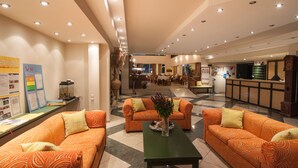 A hotel lobby with orange patterned sofas, a green table, and a reception area in the background. - Trefon Hotel Apartments and Suites (Rethymno)