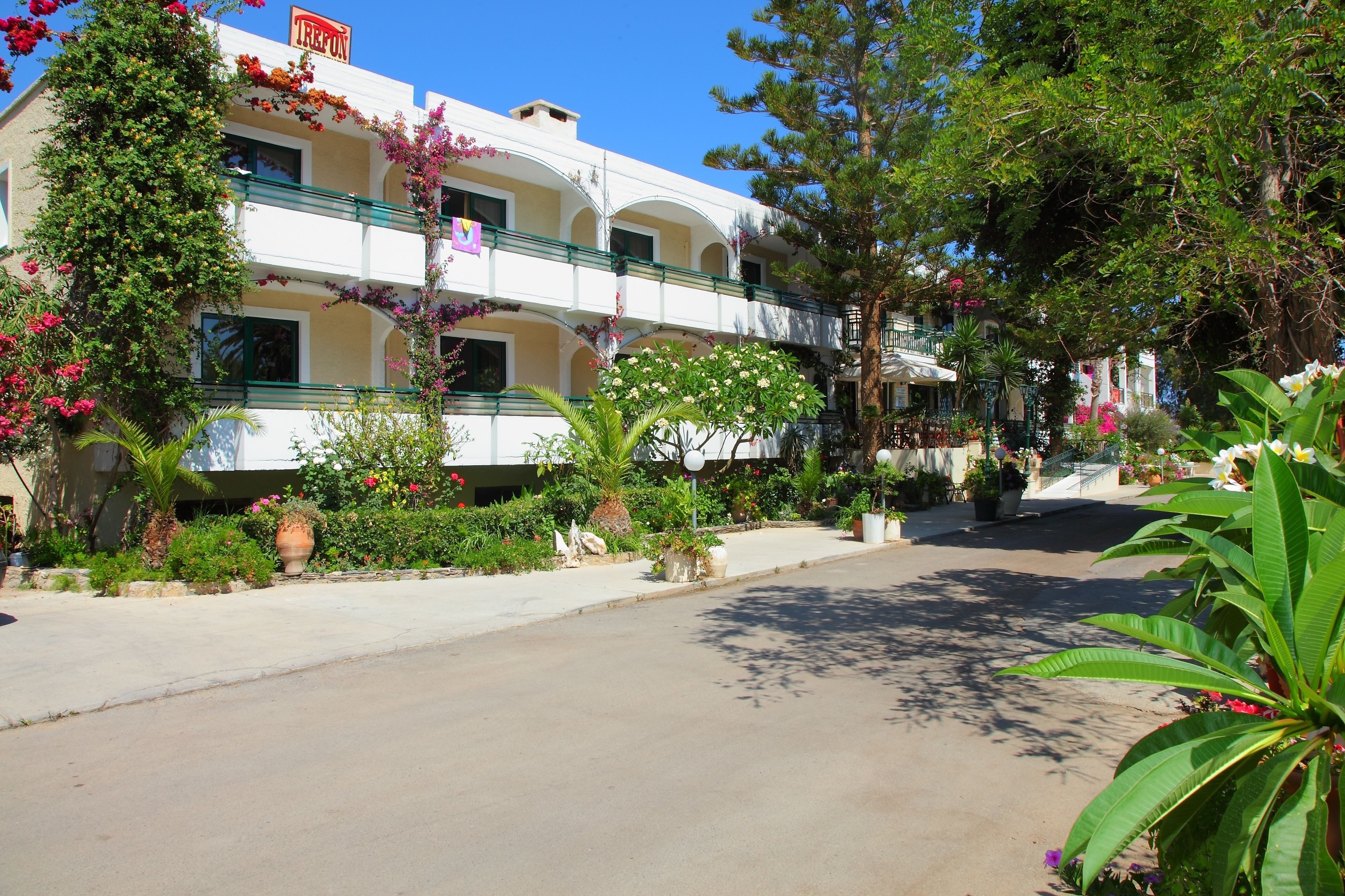 A hotel with a white facade, multiple balconies, and lush greenery.
