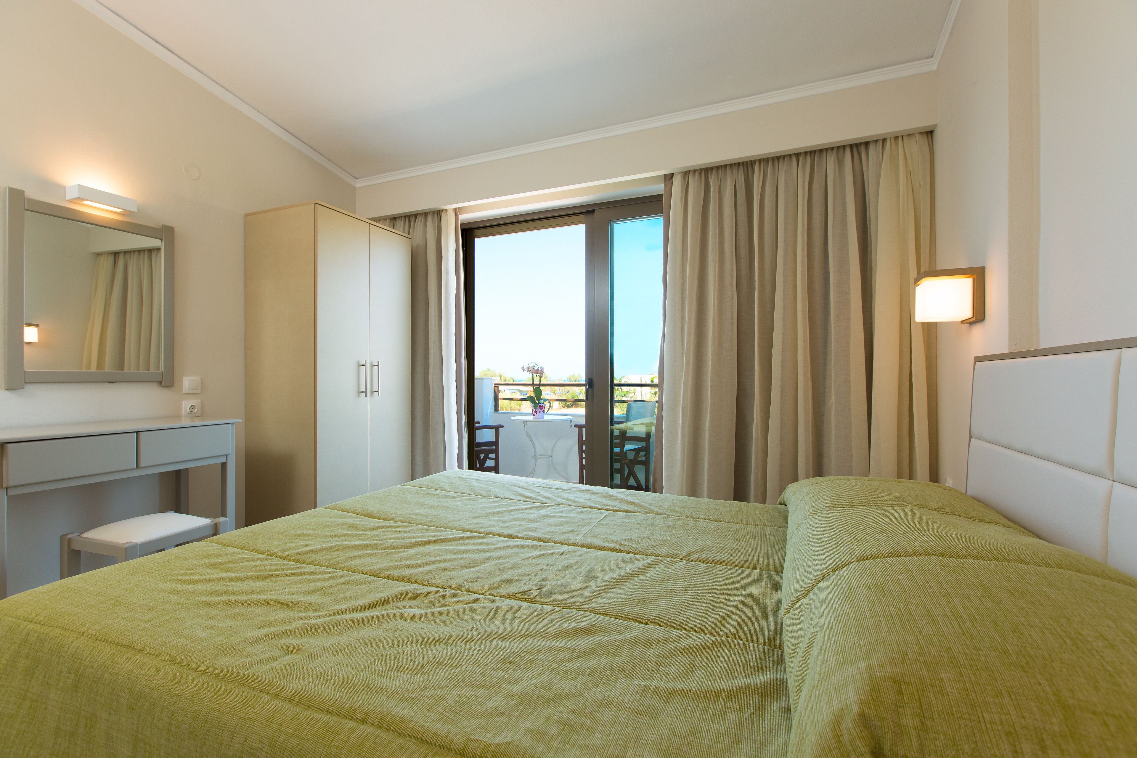 A hotel room with a bed, a desk, a chair, a mirror, and a view of the outside.