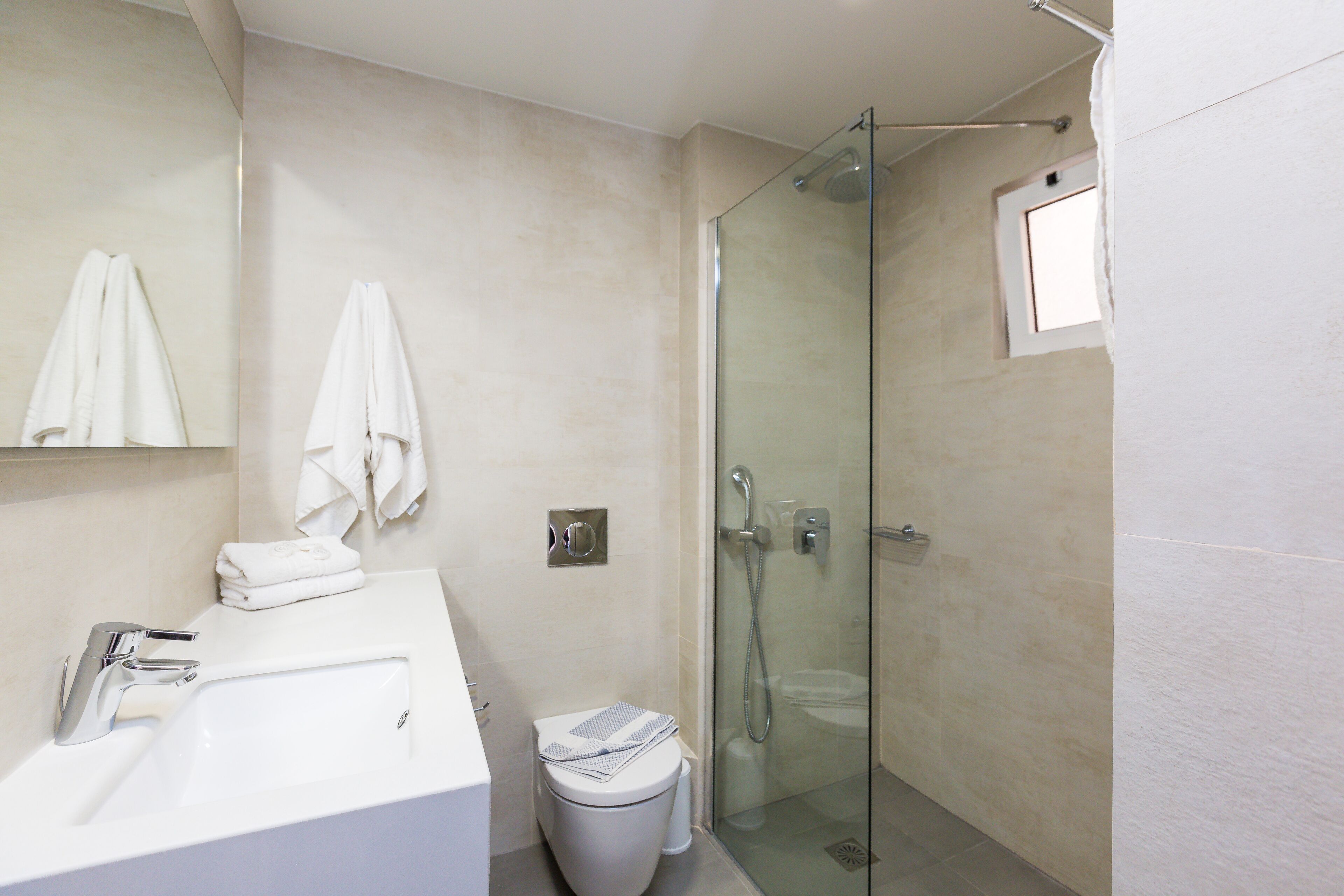 Un bany modern amb dutxa amb portes de vidre, un lavabo blanc i un vàter.