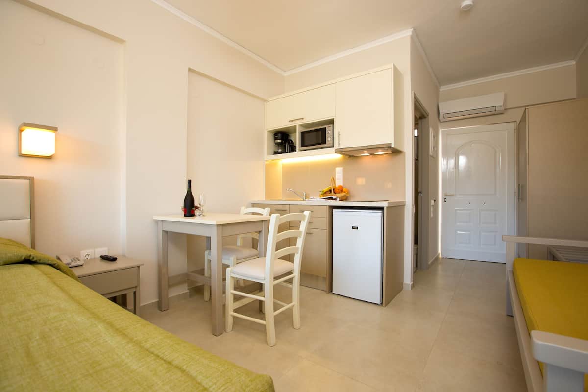 A compact hotel room with a kitchenette, a dining area, and a bed.