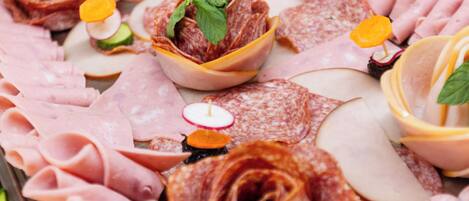 A charcuterie board with various meats, cheese, and garnishes.