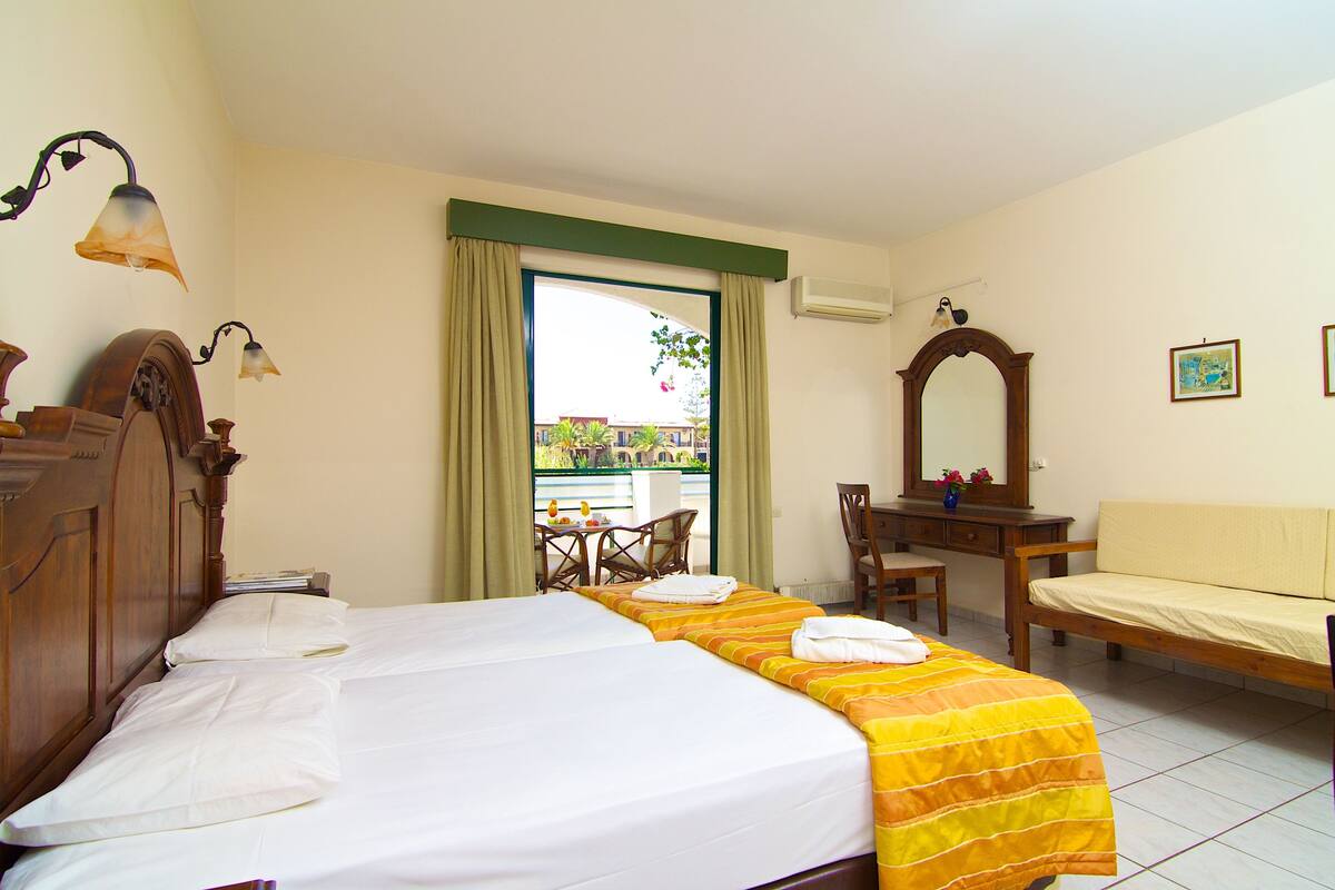A hotel room with a bed, a desk, a chair, a small table, and a window with curtains.