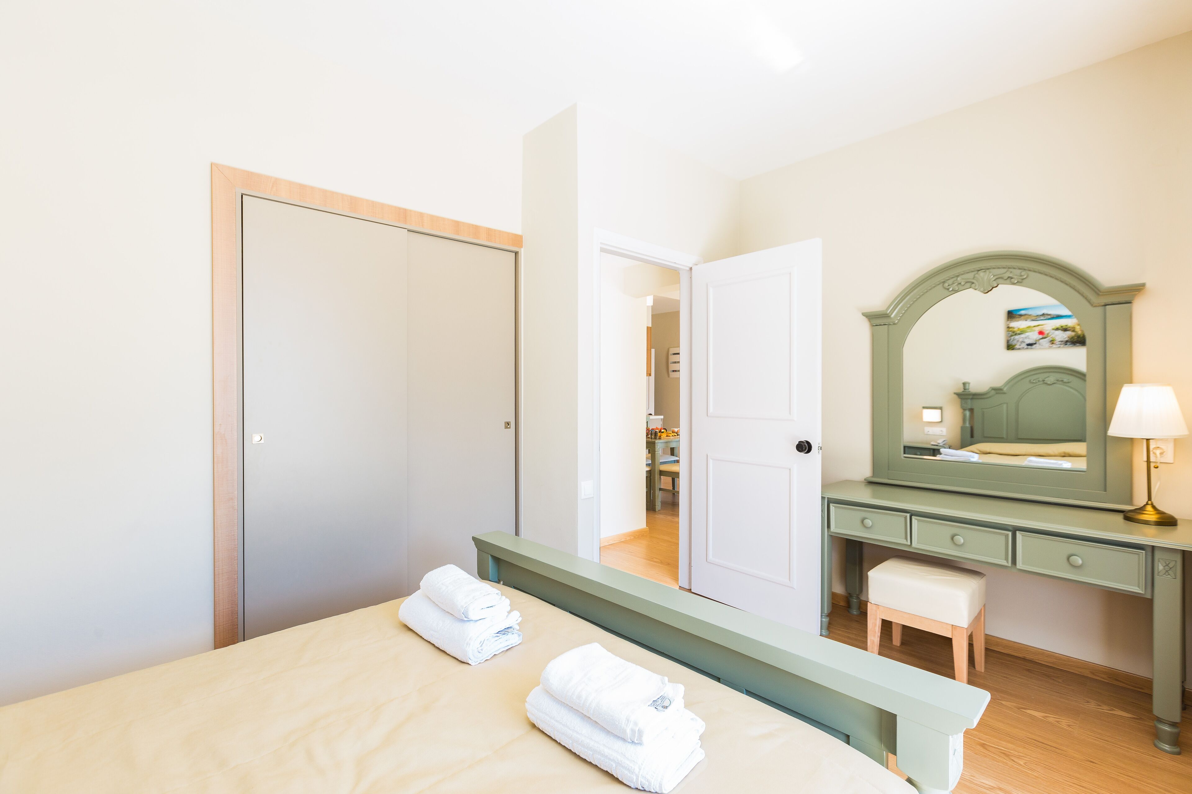 A bedroom with a bed, a nightstand, a dresser, a mirror, and a door leading to another room.