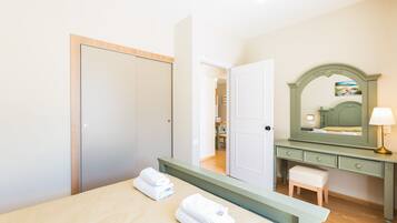 A bedroom with a bed, a nightstand, a dresser, a mirror, and a door leading to another room.