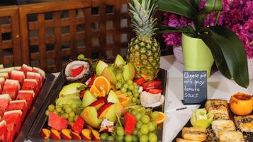 Un bufé con diversas frutas, una piña y pastel de queso con salsa de tomate picante.