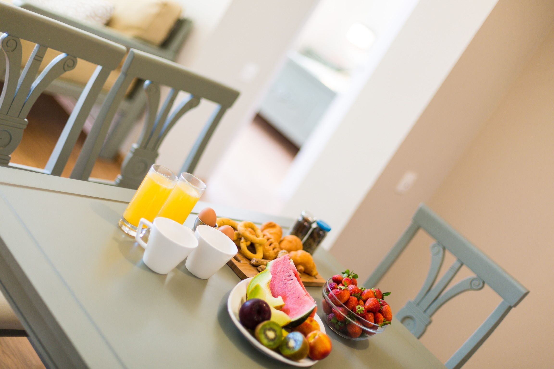A breakfast table with a plate of fruits, a glass of orange juice, and a bowl of strawberries.