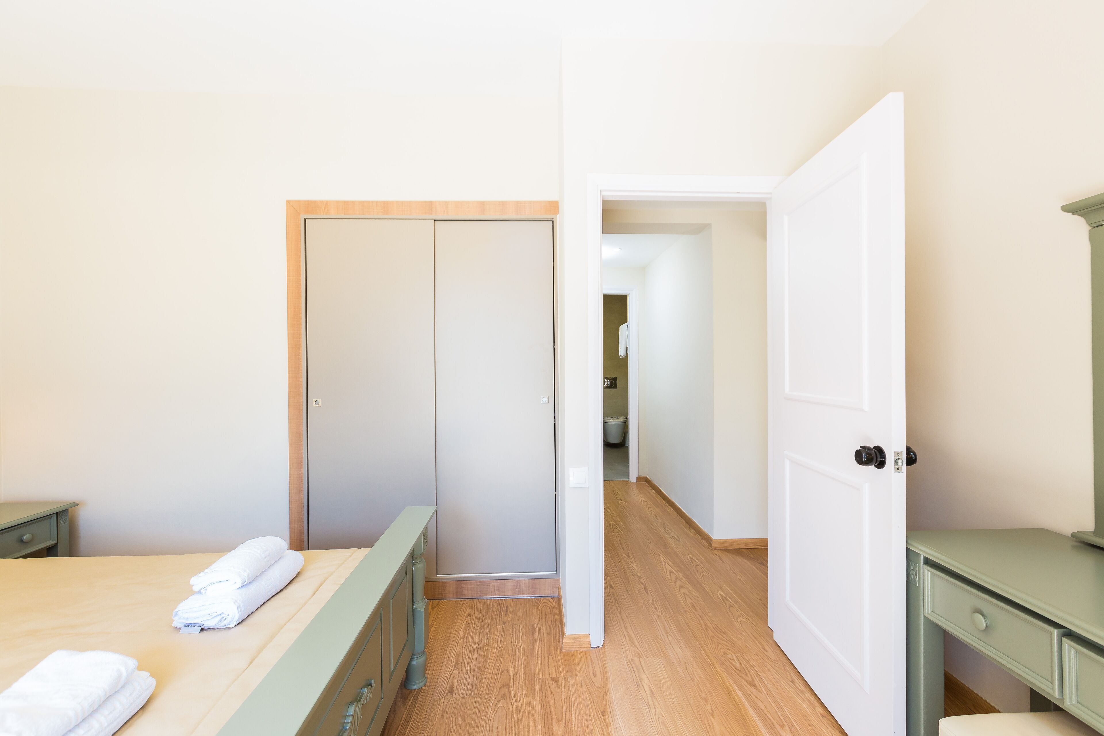 A bedroom with a bed, a wardrobe, a desk, and a door leading to another room.