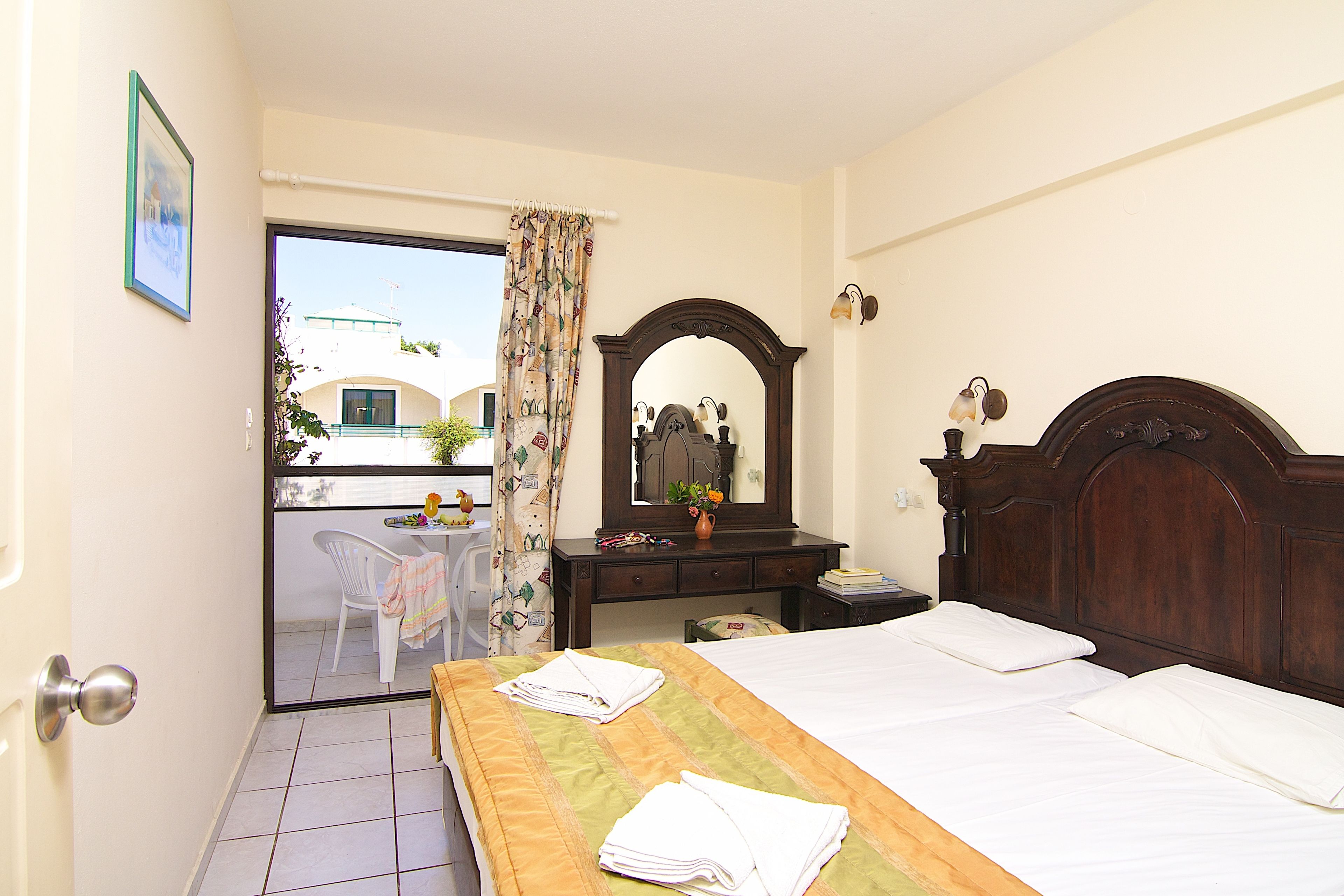 A hotel room with a bed, a wooden dresser, a mirror, and a view of the outside.