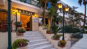 A hotel entrance with a sign reading "TREFFON" and a reception desk. There are steps leading up to the entrance, and potted plants are placed along the pathway. - Trefon Hotel Apartments and Suites (Rethymno)