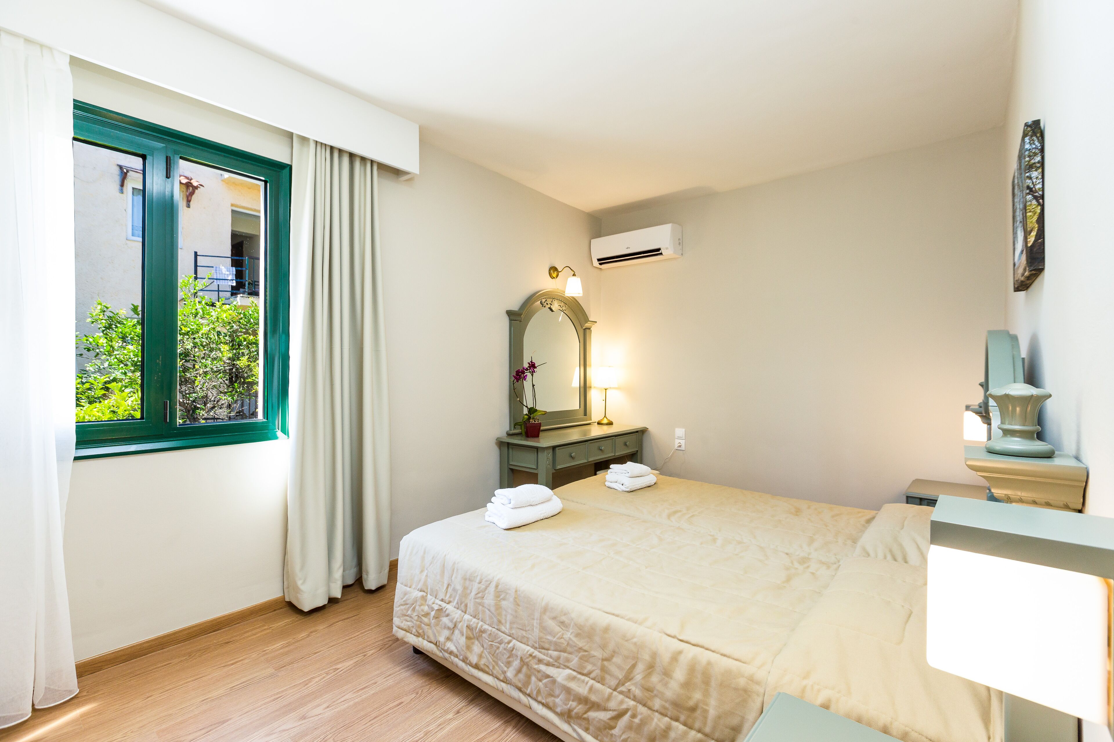 Una habitación de hotel con cama, ventana con cortinas, mesita de noche con lámpara y unidad de aire acondicionado en la pared.