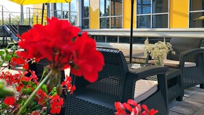 Outdoor seating with yellow umbrellas, wicker chairs, and red flowers. - Hotel Forza (Poznan)