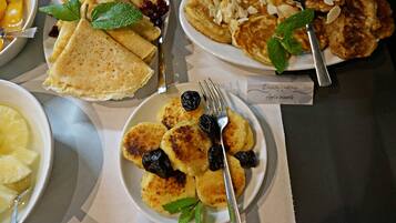 Una mesa con diferentes opciones de desayuno, como panqueques, crepes y un bol de fruta.