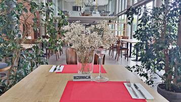 Ein Restaurant mit Holztisch, roten Platzsets, einer Blumenvase und einem Schild mit der Aufschrift 'REZERWACJA'.