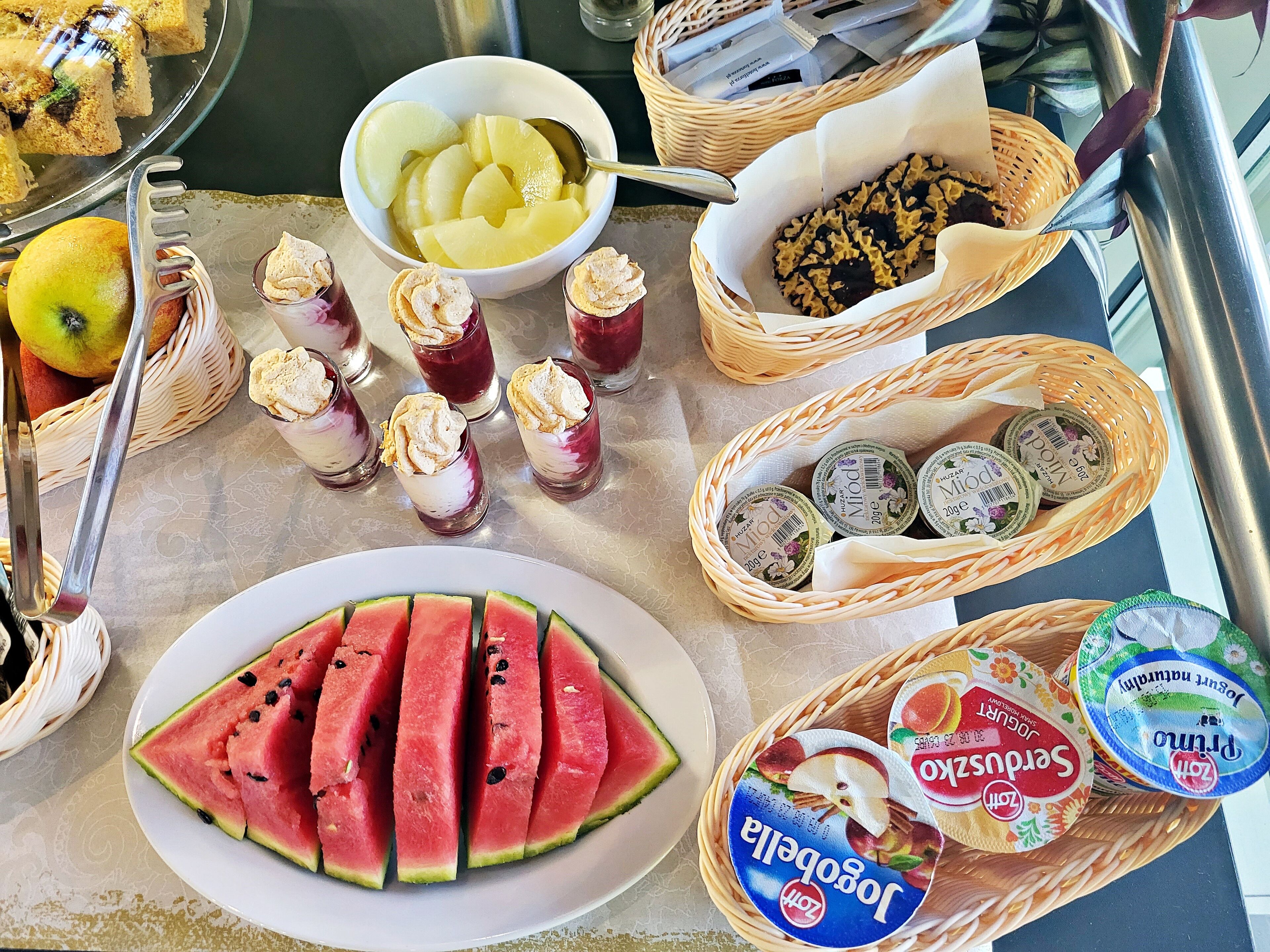 Ein Frühstücksbuffet mit verschiedenen Speisen, darunter Wassermelone, Joghurt und Fruchtparfaits.