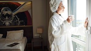 A hotel room with a bed, a nightstand, a lamp, and a window with a view of a cityscape. - Hotel Forza (Poznan)