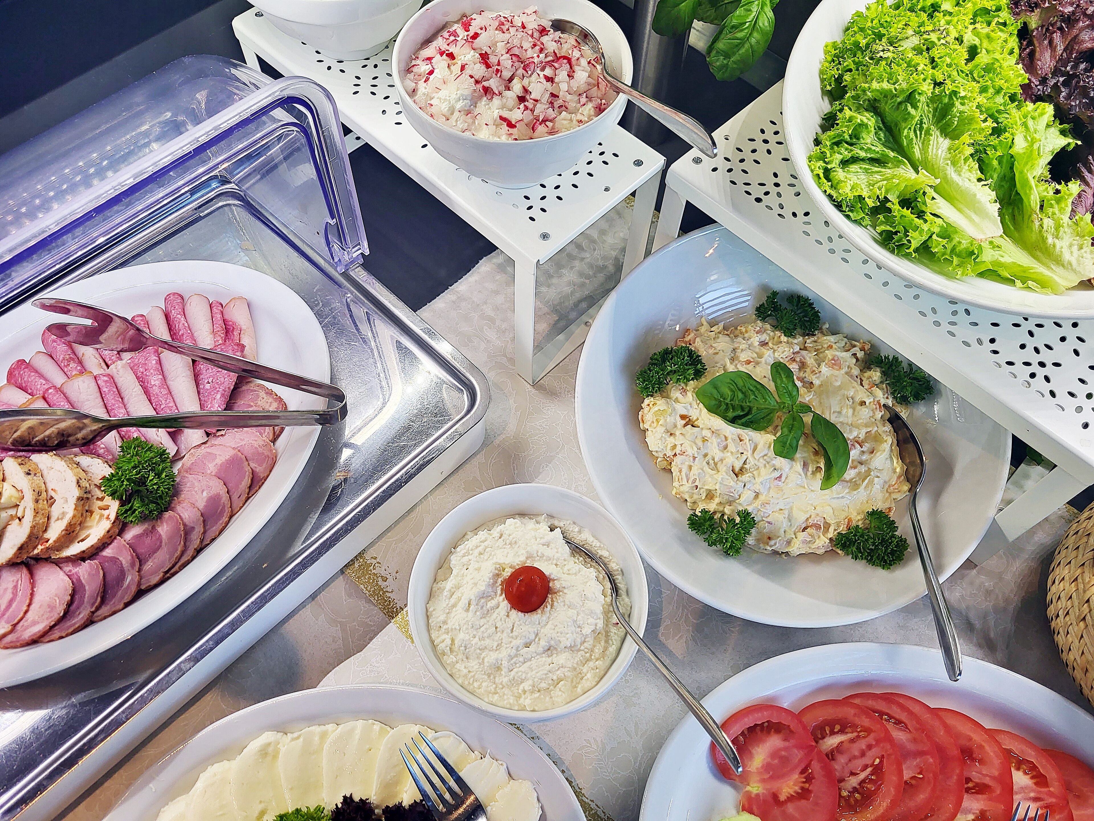 Ein Buffet mit verschiedenen Speisen, darunter Aufschnitt, Salate und Dips.
