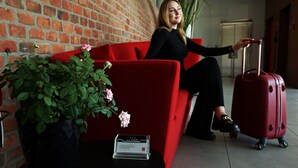 A red sofa, a potted plant with flowers, and a red suitcase in a hotel lobby. - Hotel Forza (Poznan)