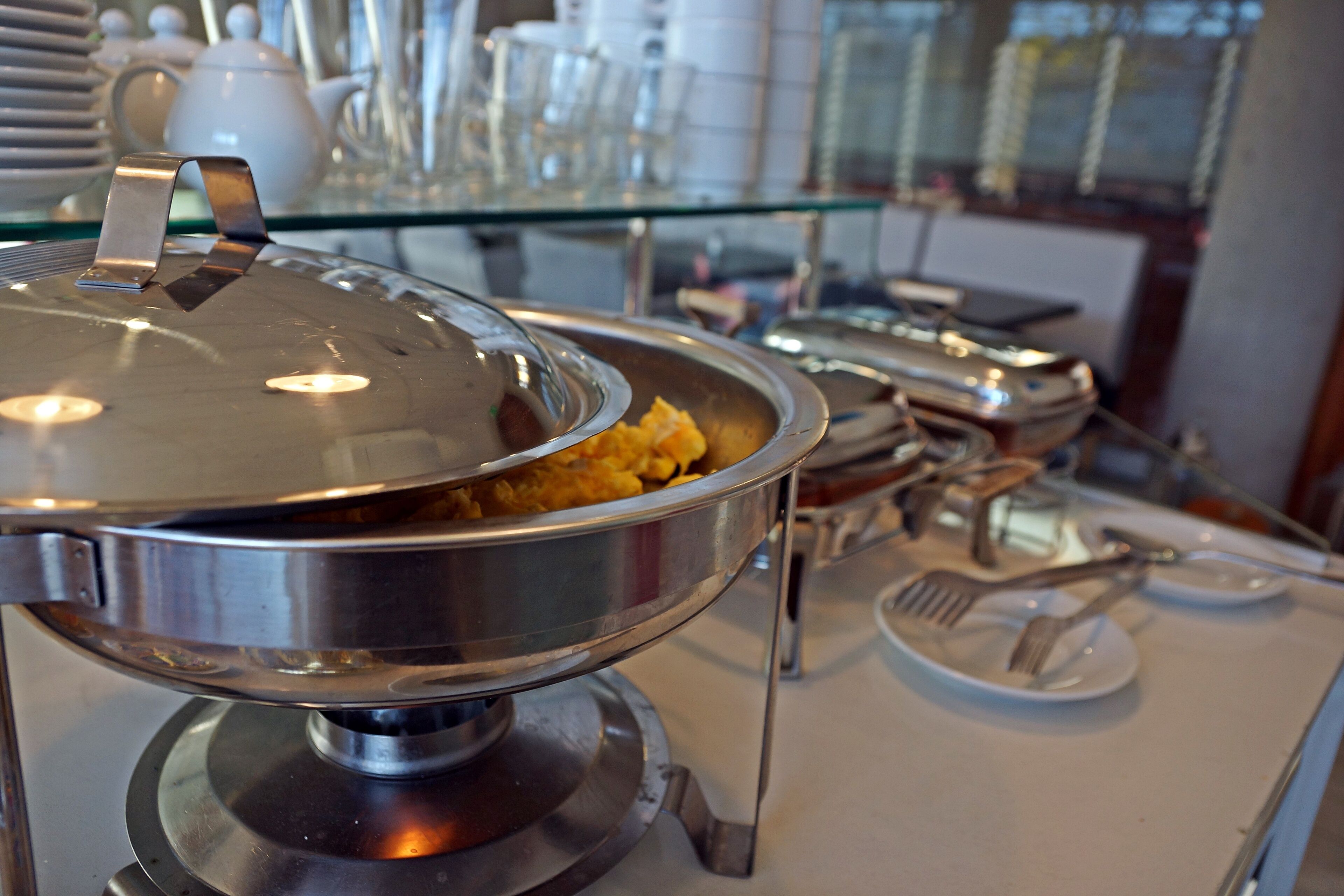Ein reichhaltiges Buffet mit einem abgedeckten Serviergeschirr, Besteck und einer Glaskühlluke im Hintergrund.