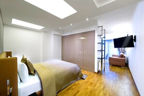 Quarto de hotel moderno com cama, secretária, televisão na parede e guarda-roupa.