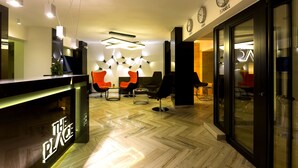 En moderne hotellobby med reception, siddeområde og ure, der viser tidszoner.