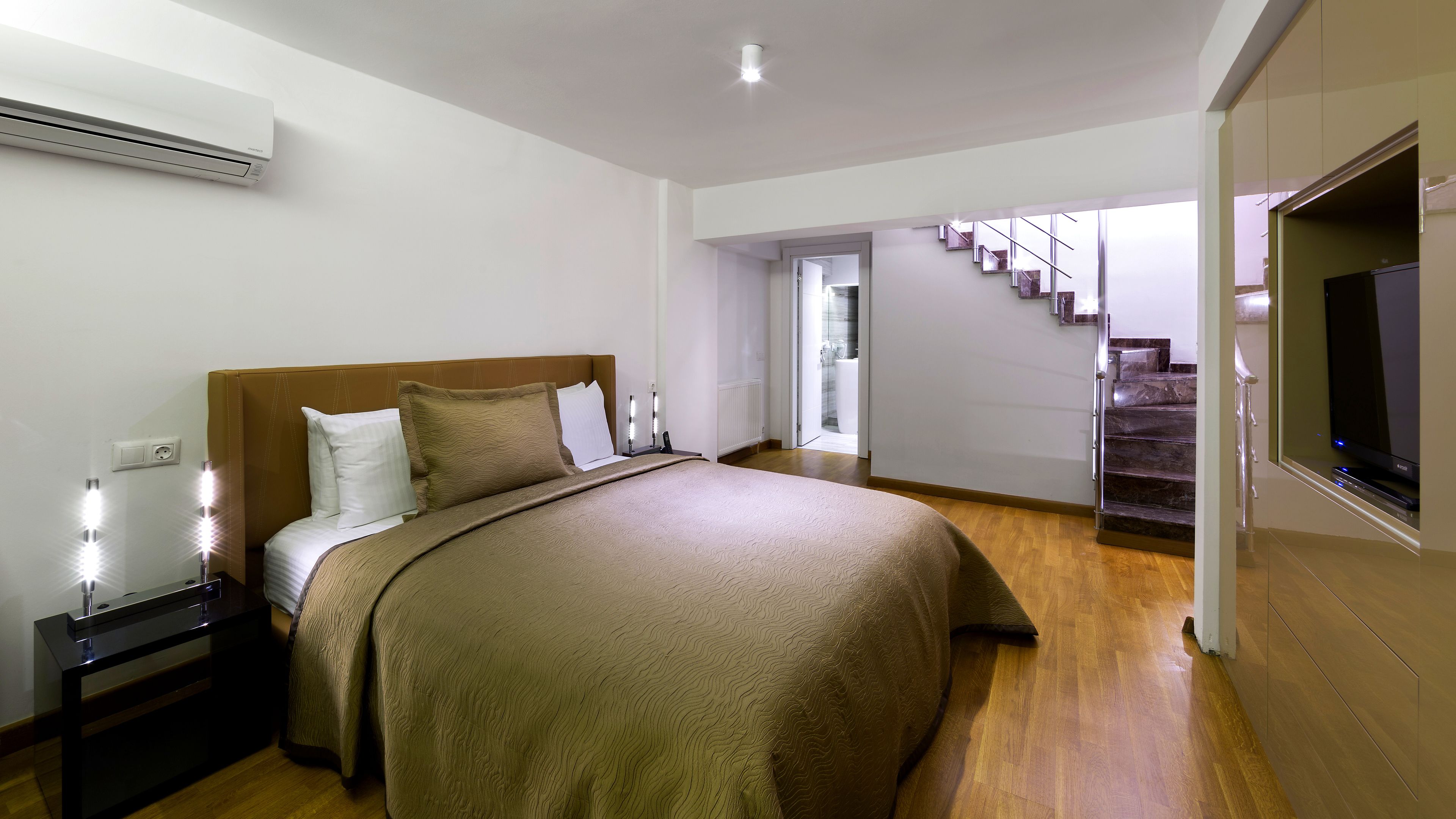 Un dormitorio moderno con una cama grande, lámparas de noche, un televisor de pantalla plana y una escalera que sube a un nivel superior.