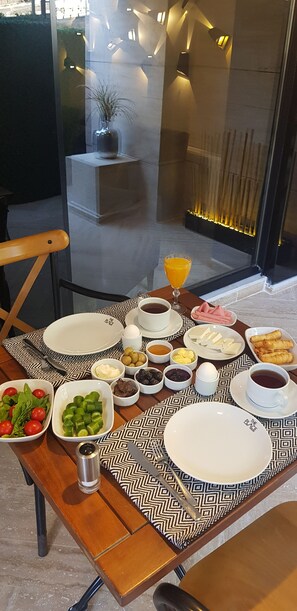 Uma mesa de café da manhã com diversos pratos, incluindo ovos, torradas e frutas, sobre uma toalha de mesa estampada.