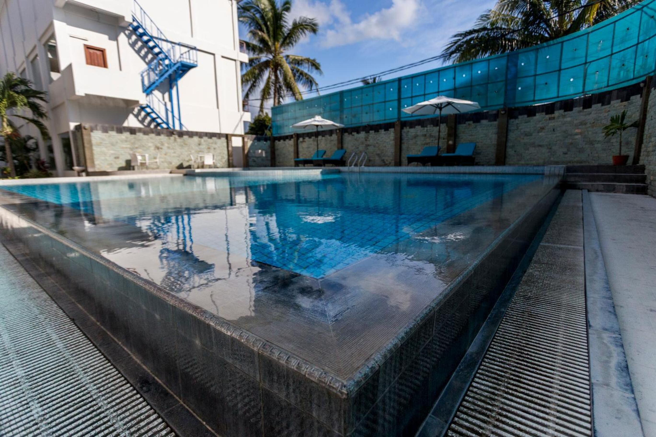 A swimming pool with a clear blue water, surrounded by a stone wall and a blue fence.