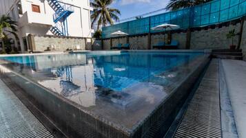 A swimming pool with a clear blue water, surrounded by a stone wall and a blue fence.