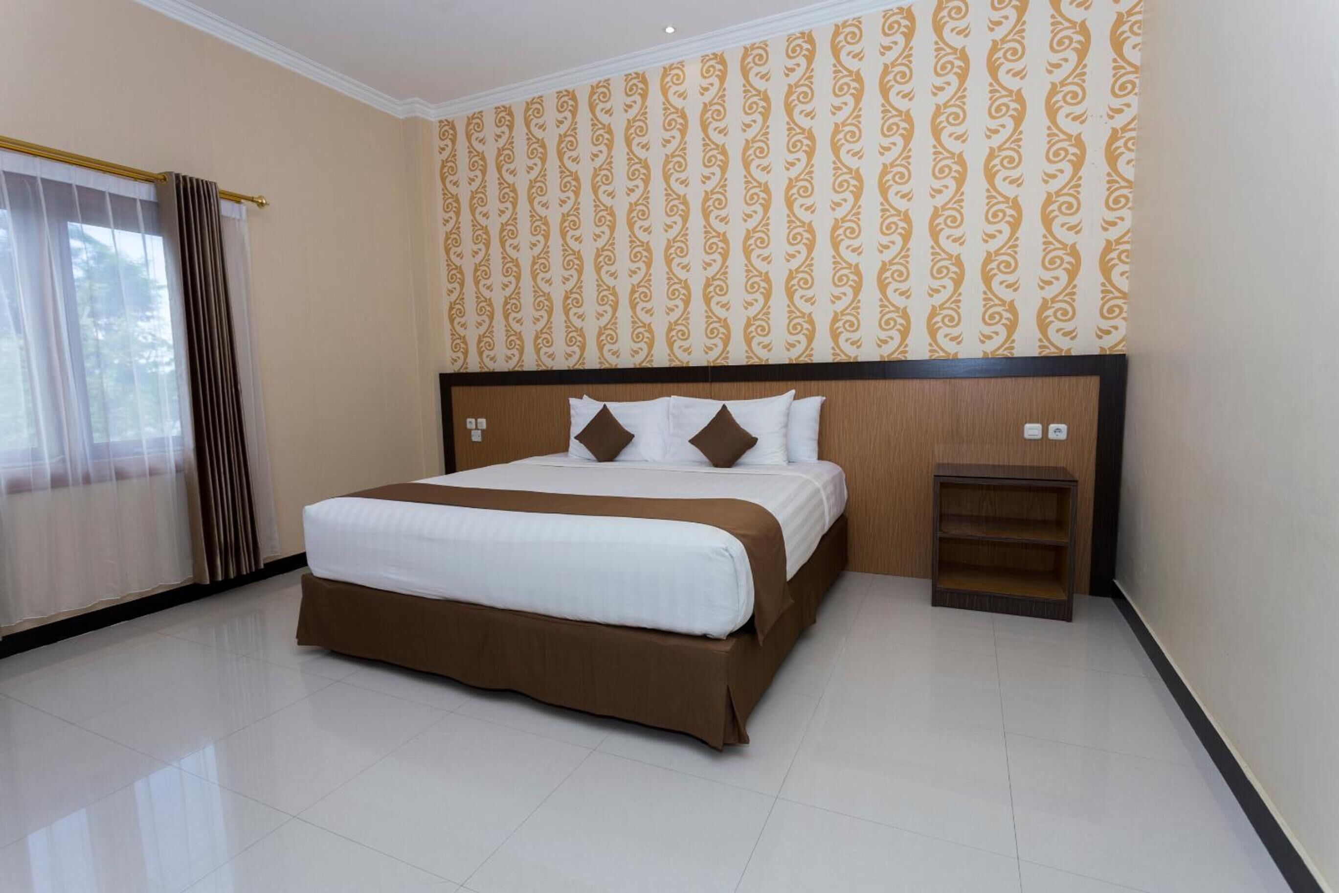 Una habitación de hotel con una cama grande, un cabecero de madera, una mesita de noche y un papel tapiz estampado.